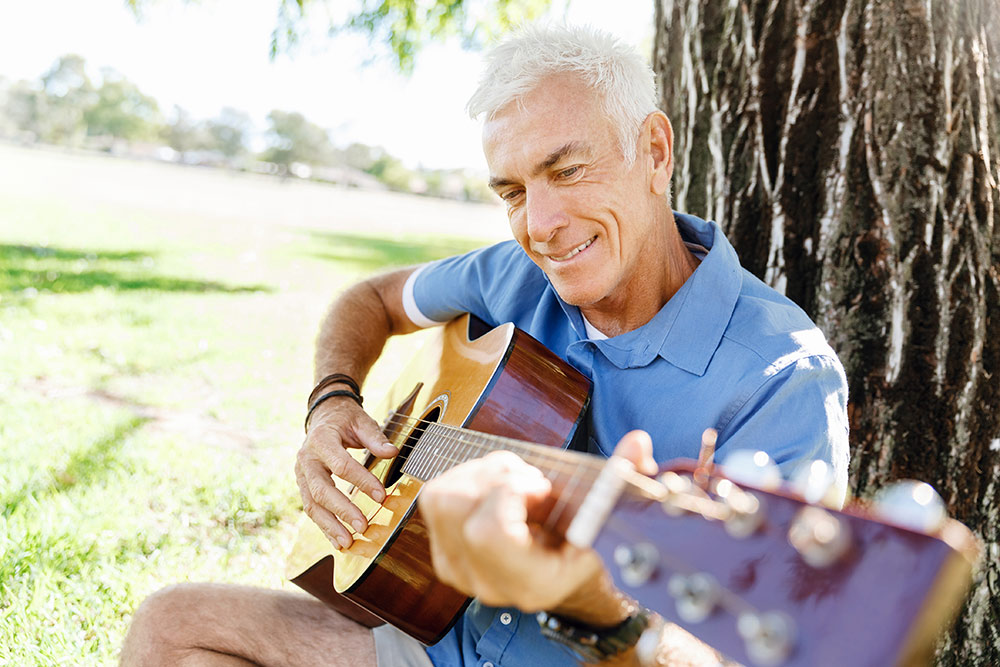 Oakleigh Macomb Senior man playing guitar outside by tree