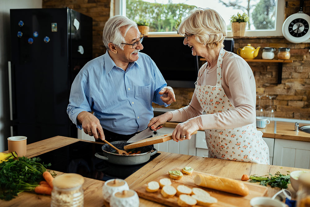 Happy senior couple smiling and cooking in kitchen
