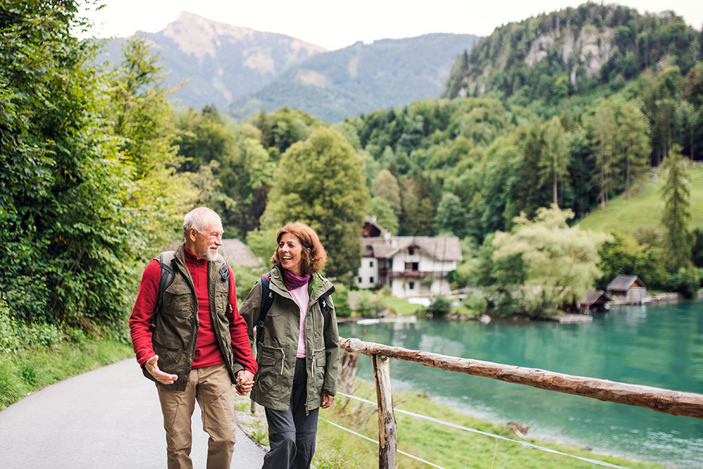 Senior couple walking near lake outside with lake house seen in the background