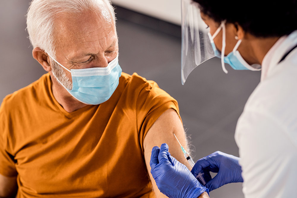 Senior man and doctor, both wear masks, man receiving vaccine from doctor