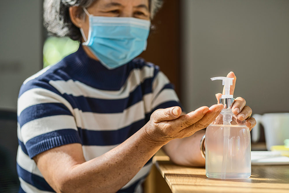 Senior woman with face mask on using hand sanitizer to stay healthy