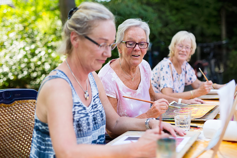 Senior women painting outside together laughing and smiling