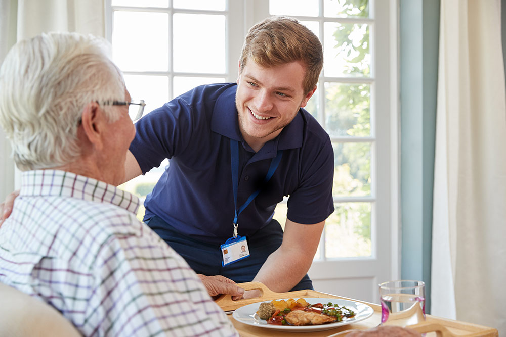 Senior man receiving food and talking with male caregiver in senior living community