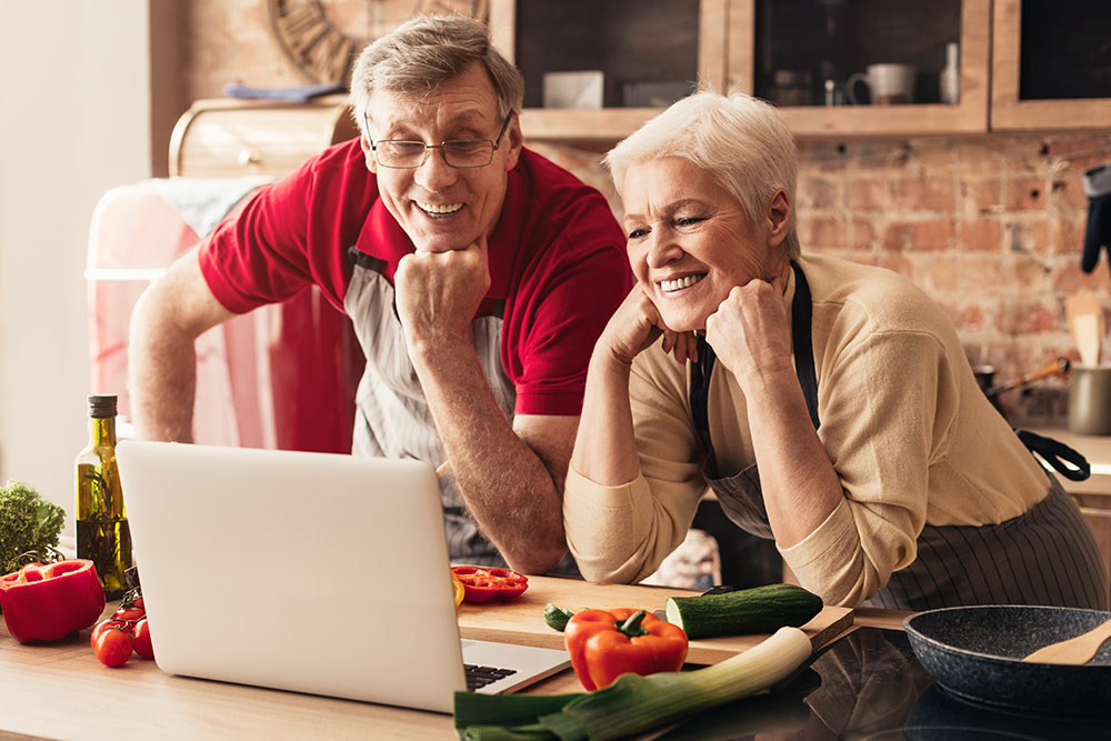 Senior couple in kitchen with laptop in virtual cooking class