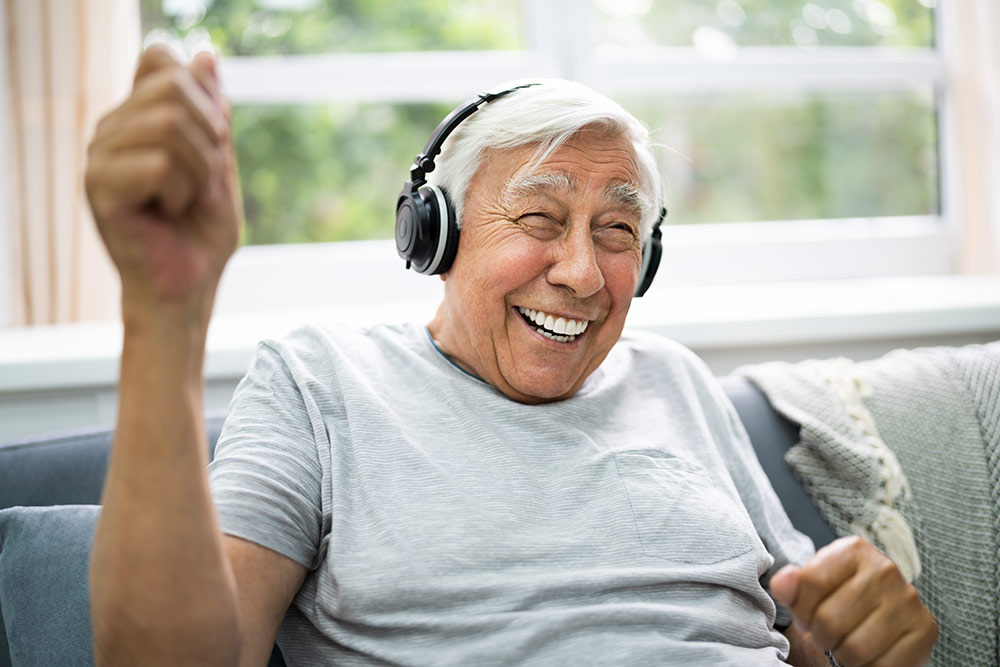 Happy senior man sitting on couch listening to music with headphones on