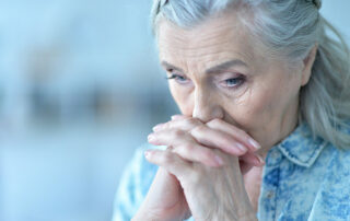 Sad senior woman looking down, holding hands by face
