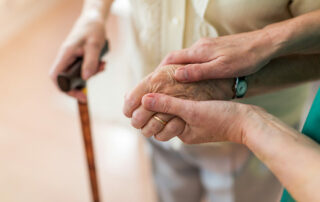 Senior hands holding cane with caregiver holding hand
