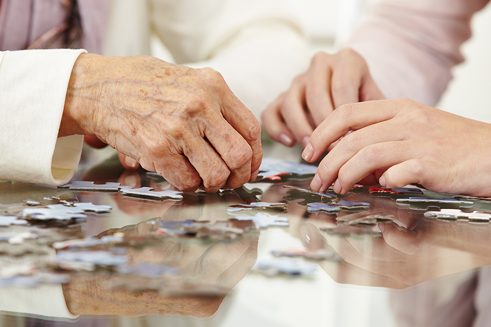 Close up of senior hands with loved one doing a puzzle on a table