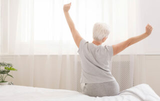 Senior woman sitting up in bed stretching, well rested