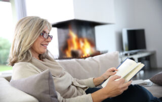 A senior woman reads a book by a fireplace
