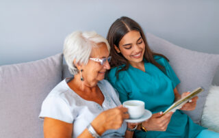 A senior woman and an assisted living nurse look at a tablet together