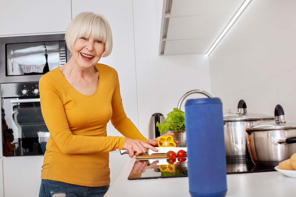 A senior woman cooks with the help of a digital assistant
