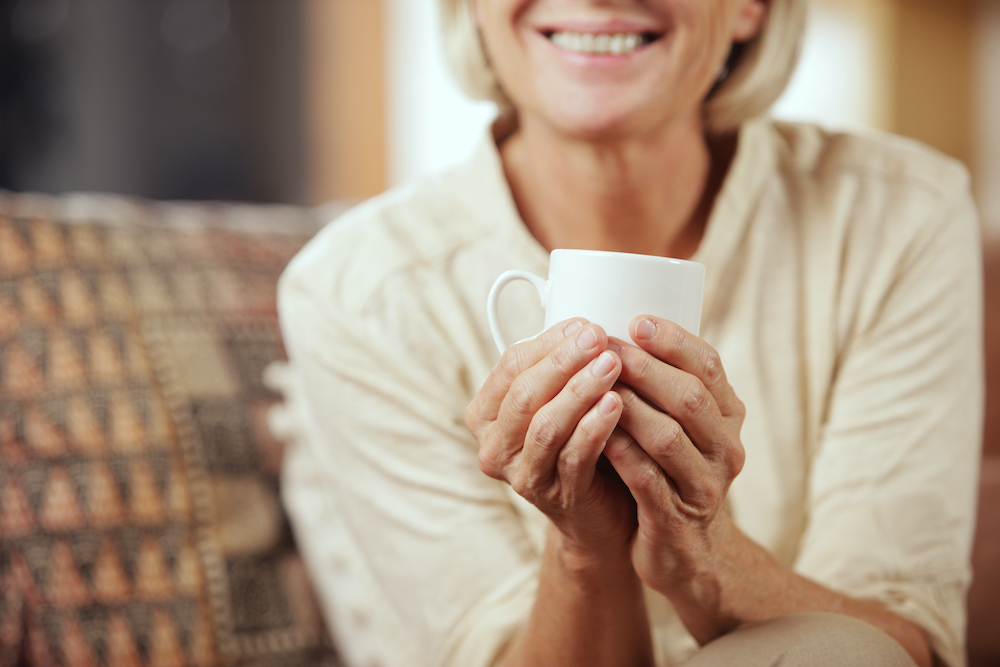 A senior woman at the senior living near me holding a mug of tea and smiling
