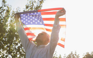 A senior man holding up an American flag outdoors