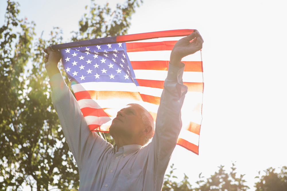 A senior man holding up an American flag outdoors