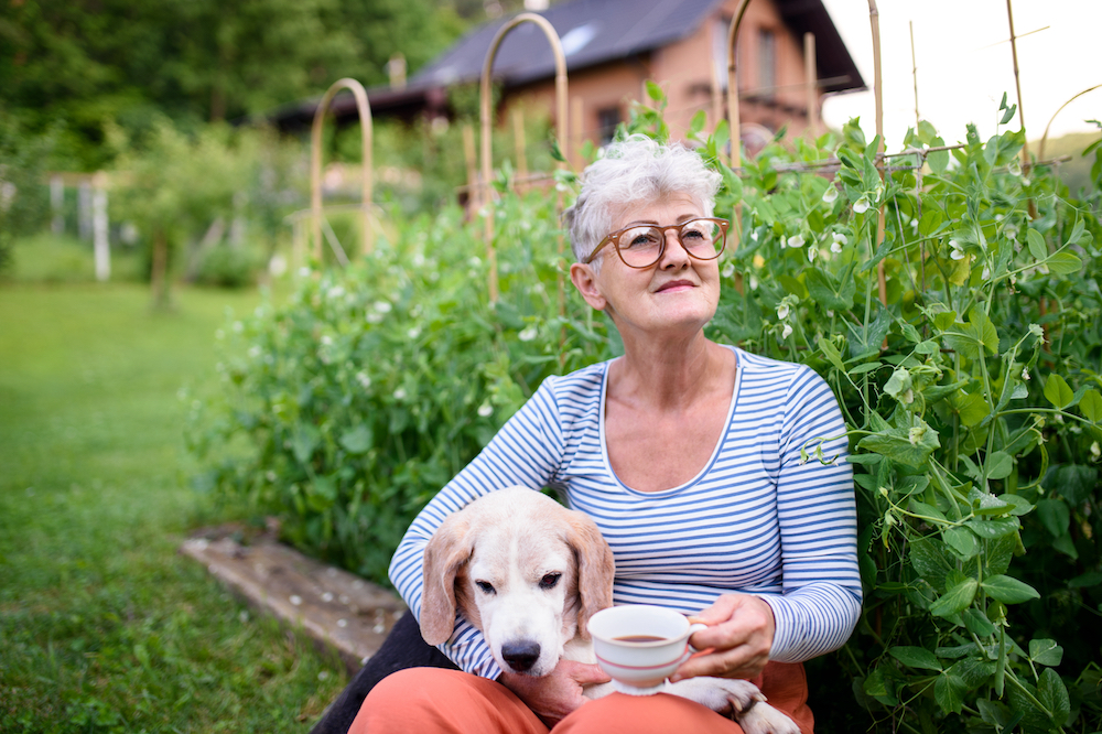A senior woman drinking tea outdoors with her dog
