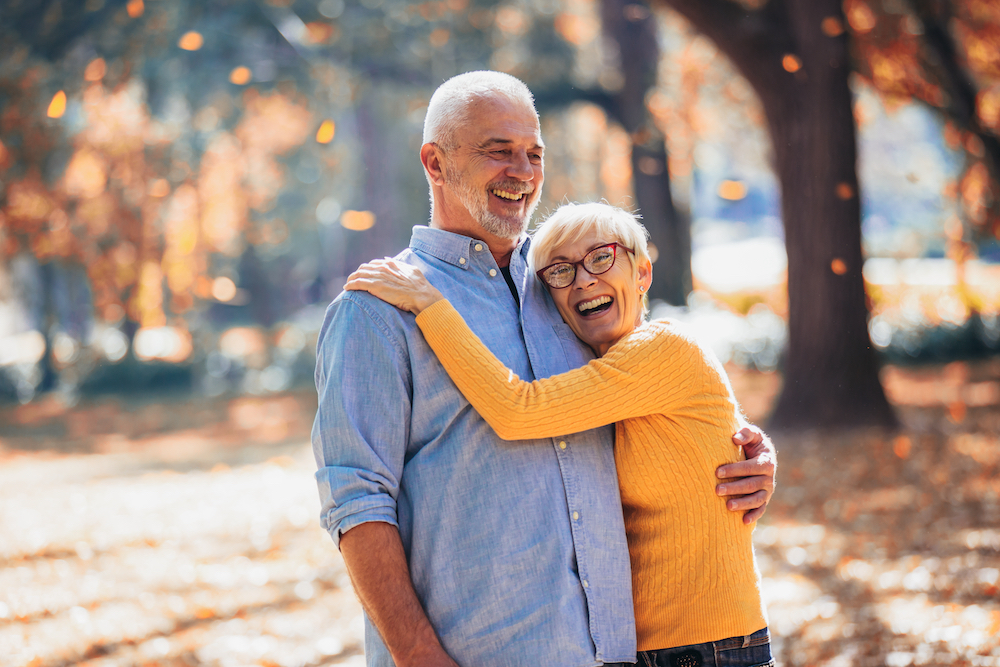 A senior couple shares a hug while walking outdoors during the fall season