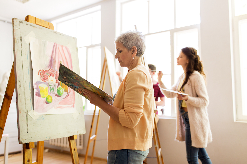A senior woman painting on a canvas during art class