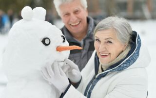 A happy senior couple builds a snowman outside