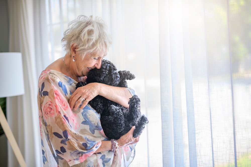 A senior woman hugs her black dog at the best assisted living in Michigan