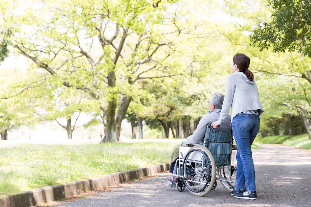 A senior man in a wheelchair and his caregiver going for a walk through the park